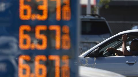 Imagen de una torre de precios y en el fondo el conductor de un vehículo.