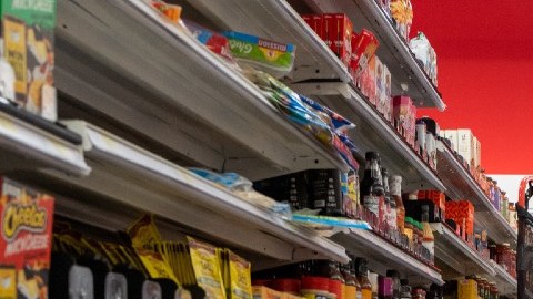 una persona en un pasillo de supermercado con algunos estantes vacíos.