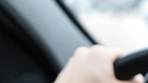 Una persona sostiene en una de sus manos un teléfono móvil con un logotipo de Uber en la pantalla, mientras conduce un auto.