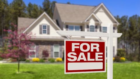 un letrero de venta de vivienda frente a una casa de dos niveles y un jardín.