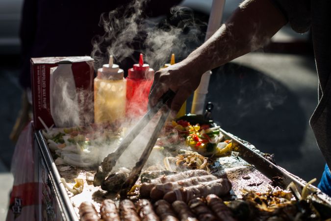 A street vendor prepares hot dogs on a sidewalk off N Main street, in front of Placita Olvera, Downtown Los Angeles on March 10, 2019. - On January 1, 2019, the Safe Vending Act (SB946) went into effect in the state of California prohibiting the arrest or finning of street vendors and leaving to municipalities the power to establish permits, sanitation and security issues. The Los Angeles County has set a year to negotiate with vendors the terms on which the law is going to be applied. Some 50,000 street vendors are estimated to work in Los Angeles, a $504 million industry according to a 2015 study by the Economic Roundtable. The LA County issued a municipal ordinance that designates specific areas where the vendors must operate. The ordinance does not include areas such as Memorial Coliseum, the Staples Center, Dodger Stadium, Rose Bowl Stadium and the Hollywood Walk of Fame. Street vendors have mixed feelings about the legalization of their work. At the same time they feel freed of being against the law and harassed by police giving them tickets and seizing their goods; they are concerned about having to abide to health regulations, permits and limited areas. (Photo by Agustin PAULLIER / AFP) (Photo credit should read AGUSTIN PAULLIER/AFP via Getty Images)