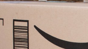Tres cajas de cartón con cintas de seguridad de Amazon apiladas frente a una puerta de madera blanca.