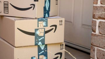 Tres cajas de cartón con cintas de seguridad de Amazon apiladas frente a una puerta de madera blanca.