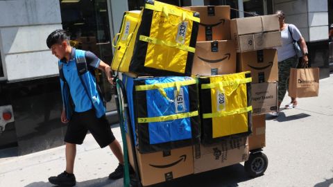 Un trabajador de Amazon vestido con el uniforme de reparto jala una tarima móvil repleta de cajas de Amazon.