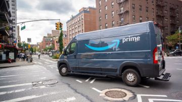 Una camioneta de color azul oscuro con los logotipos de Amazon da vuelta en una calle.