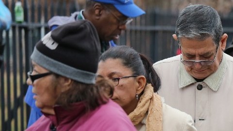 Personas que cargan bolsas hacen fila para recibir ayudas de alimentos.