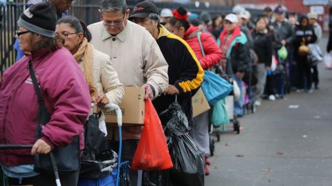 Personas que cargan bolsas hacen fila para recibir ayudas de alimentos.