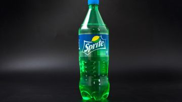 Imagen de una botella de color verde con etiquetas de la marca Sprite, en un fondo negro.