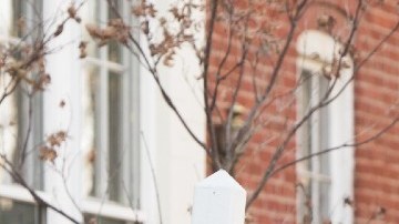 letreros de venta de vivienda en color azul se ven frente a casas y en el fondo una bandera de los Estados Unidos.