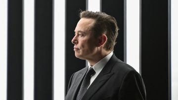 Elon Musk, CEO de Tesla, parado con un traje negro frente a un muro con luz blanca.