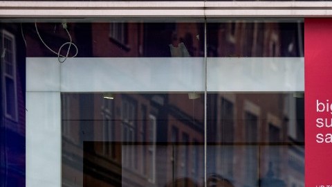 Un hombre camina frente a una tienda de la marca GAP, en la que hay letreros de rebajas.