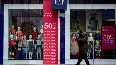 Un hombre camina frente a una tienda de la marca GAP, en la que hay letreros de rebajas.