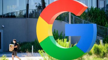 Un logotipo de Google se ve frente a un edificio de oficinas, mientras una persona camina con una caja en las manos.