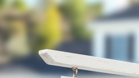 Un letrero de venta en madera frente a una vivienda en segundo plano fuera de foco.