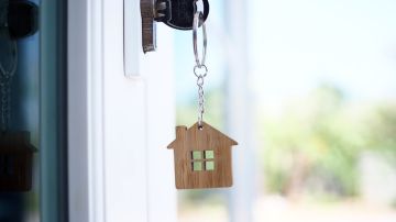 Unas llaves que cuelgan de la chapa de una puerta, con un llavero en forma de casa.