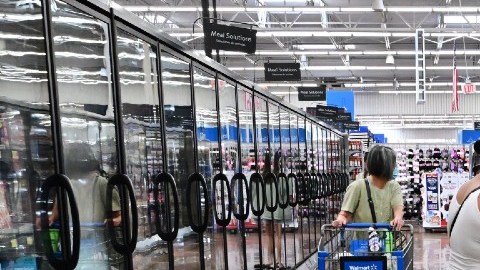 Tres mujeres escogen productos en un pasillo de un supermercado, en el que se ven tres carritos de supermercado de Walmart.