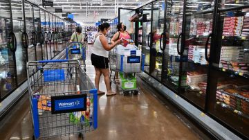 Tres mujeres escogen productos en un pasillo de un supermercado, en el que se ven tres carritos de supermercado de Walmart.