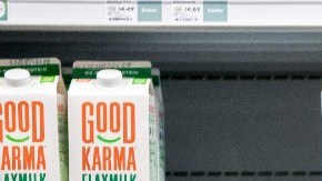 Una mujer empuja un carrito de supermercado frente a estantes en donde están colocados envases de leche.