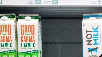 Una mujer empuja un carrito de supermercado frente a estantes en donde están colocados envases de leche.