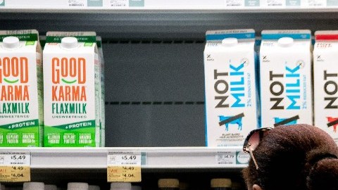 Una mujer empuja un carrito de supermercado frente a estantes en donde están colocados envases de leche.