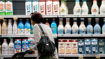 Una mujer empuja un carrito de supermercado frente a estantes en donde están colocados envases de leche.