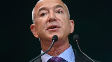 Imagen de Jeff Bezos, vestido con un traje oscuro y una camisa color azul, parado frente a un estrado con dos micrófonos.