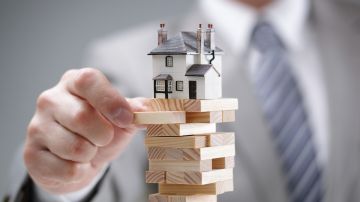 Imagen de una vivienda en miniatura sobre una torre de cubos de madera y una mano que está retirando uno.