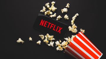 La pantalla de una tablet con un logotipo de Netflix, entre palomitas de maíz regadas y un vaso volteado.