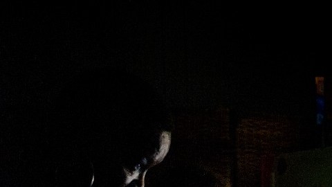 Una mujer negra que carga a su bebé se acerca a una ventana y a un ventilador para refrescarse.