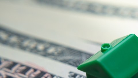 Una casa de plástico verde en miniatura que está colocada sobre un billete de $50 dólares.