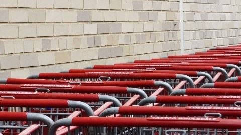 Una persona empuja un carrito de supermercado justo a un costado de una fila de varios otros carritos empotrados unos con otros.