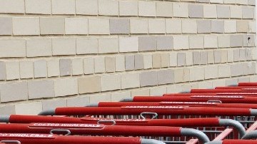 Una persona empuja un carrito de supermercado justo a un costado de una fila de varios otros carritos empotrados unos con otros.