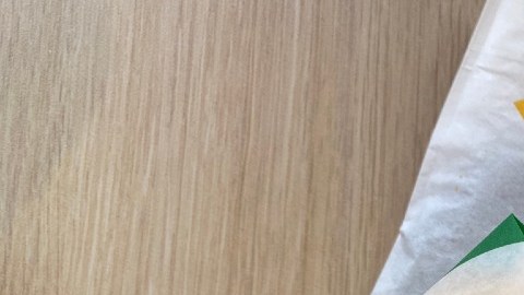 Imagen de dos sandwich de la marca Subway envueltos en papel con colores verde y amarillo, colocados sobre una mesa de madera.