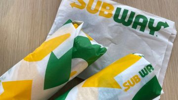 Imagen de dos sandwich de la marca Subway envueltos en papel con colores verde y amarillo, colocados sobre una mesa de madera.
