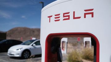 Una estación de carga eléctrica de la marca Tesla con un vehículo de la misma marca en el fondo.