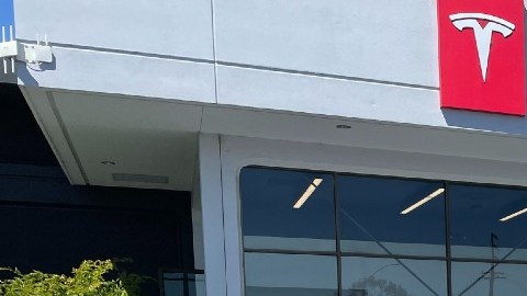 Imagen de varios autos de la marca Tesla en color blanco, estacionados frente a una distribuidora de la marca.