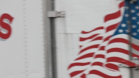 Imagen de dos trabajadores que cargan cosas, entre camiones.