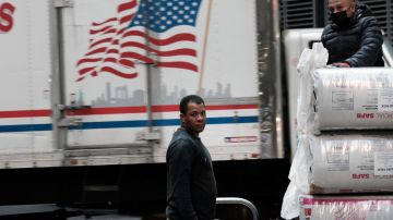 Imagen de dos trabajadores que cargan cosas, entre camiones.