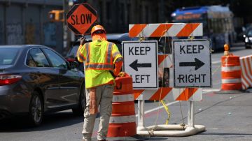 Un trabajador sostiene una señal de tránsito en medio del cierre de una calle por obras.