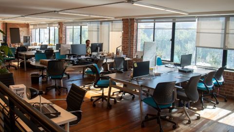 Un oficina con estaciones de trabajo y computadoras vacías, con una persona que ocupa un sitio de trabajo.