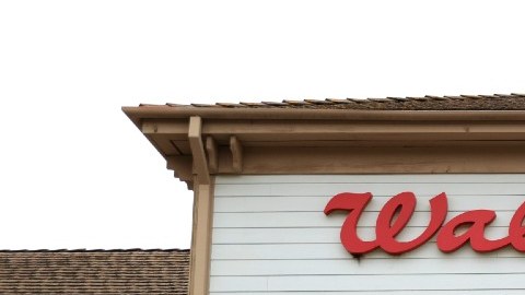 La fachada de un local de la farmacia Walgreens con una persona que sale del local y un vehículo de color blanco estacionado.