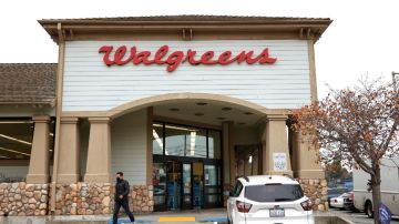 La fachada de un local de la farmacia Walgreens con una persona que sale del local y un vehículo de color blanco estacionado.