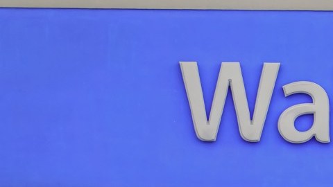 Dos personas salen de una tienda Walmart y caminan en el estacionamiento mientras empujan un carrito de supermercado.
