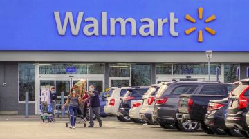 Dos personas salen de una tienda Walmart y caminan en el estacionamiento mientras empujan un carrito de supermercado.
