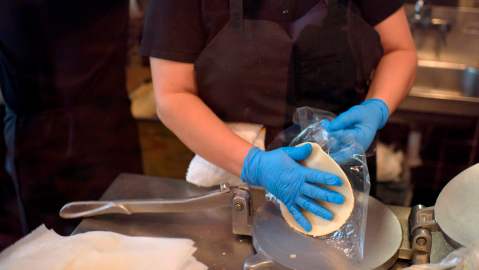 A worker at The Original Ninfa's wears gloves while making tortillas for takeout orders amid the novel coronavirus pandemic on May 1, 2020 in Houston, Texas. - Texas on Friday became the largest US state to begin easing coronavirus lockdown measures despite reporting a single-day high in deaths. Stores, restaurants, movie theaters, malls, museums and libraries were allowed to reopen in the Lone Star State but with limited occupancy -- just 25 percent of their capacity. (Photo by Mark Felix / AFP) (Photo by MARK FELIX/AFP /AFP via Getty Images)