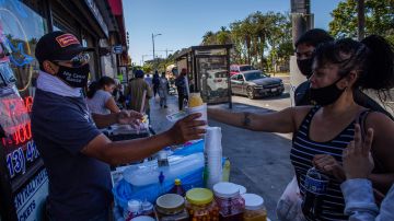 A street vendor sells a snow cone to customers in MacArthur Park, Los Angeles on May 21, 2020. - Undocumented immigrants impacted by the corornavirus shutdown can apply for California coronavirus emergency assistance plan for undocumented people put in place by Governor Gavin Newsom in April. (Photo by Apu GOMES / AFP) (Photo by APU GOMES/AFP via Getty Images)