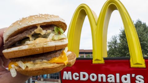 Una persona muestra una big mac con la mano frente a un logotipo de McDonald's.