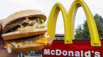 Una persona muestra una big mac con la mano frente a un logotipo de McDonald's.