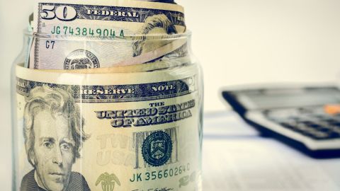Imagen de un frasco en el que se guardan billetes, con una calculadora en el fondo.