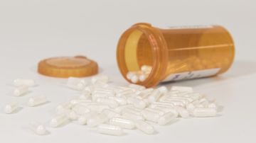 Imagen de un contenedor de medicamentos en color naranja con varias pastillas regadas.